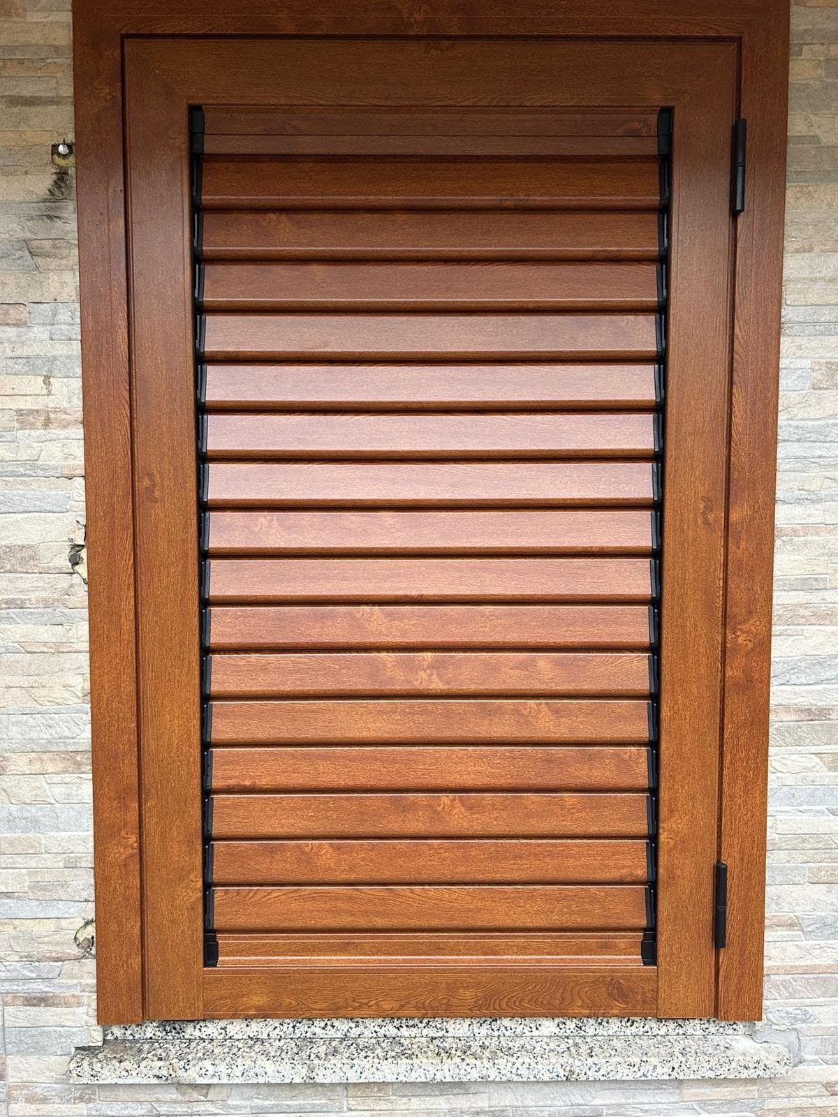Dettaglio persiana in legno effetto noce su parete rivestita in pietra