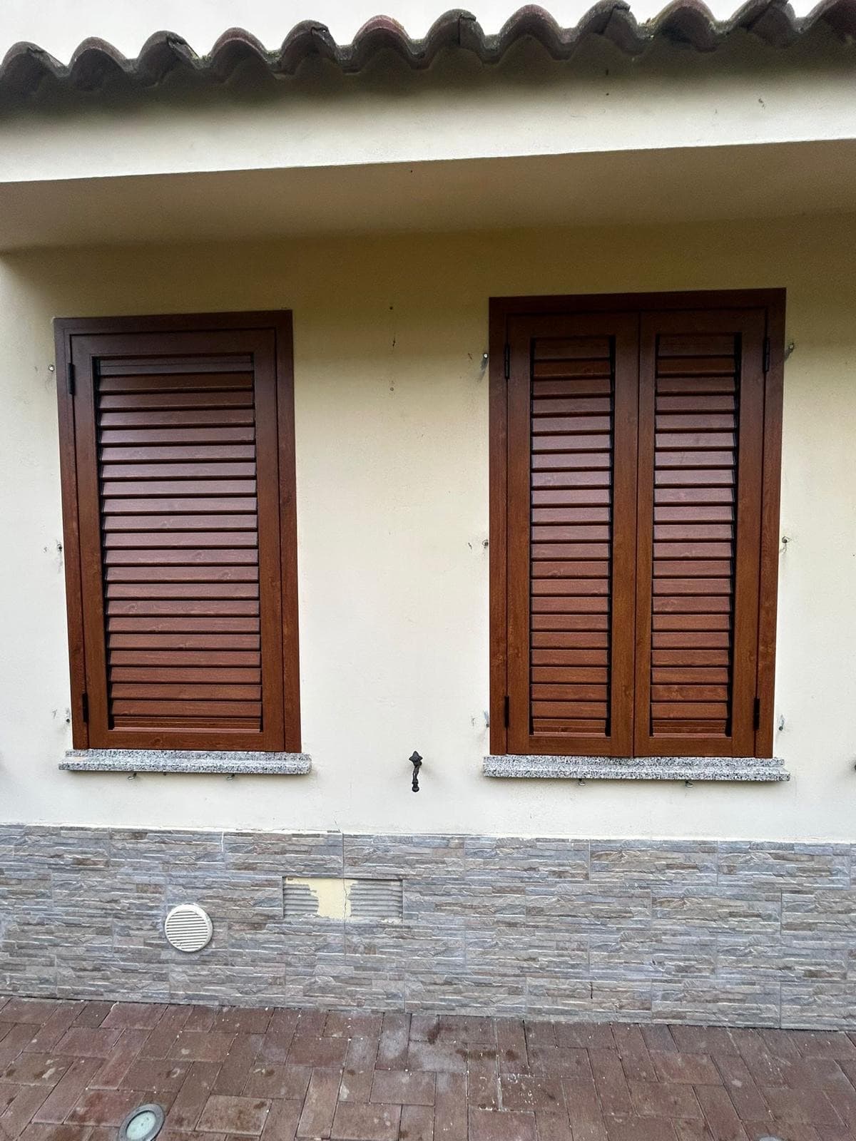Persiane in legno installate su due finestre, facciata con zoccolatura in pietra